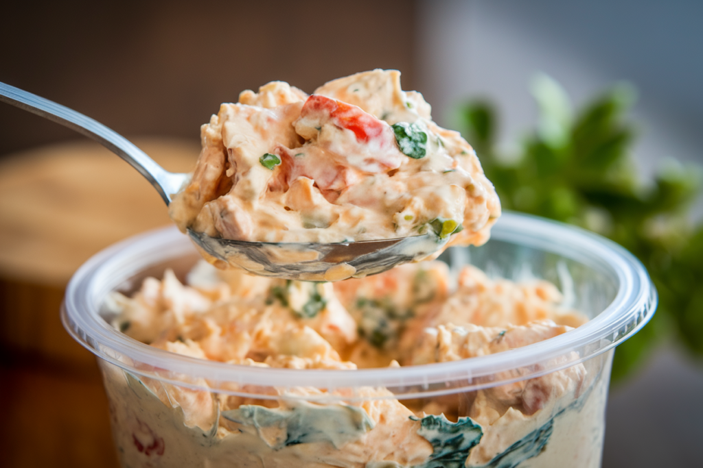 A spoon scooping chicken salad from a small container.